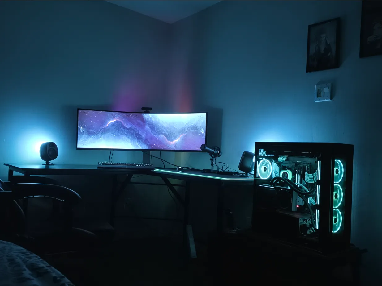 My workstation: a curved ultrawide monitor flanked by bookshelf speakers and a broadcast microphone, with a glass-panel PC tower lit in cyan to the right.